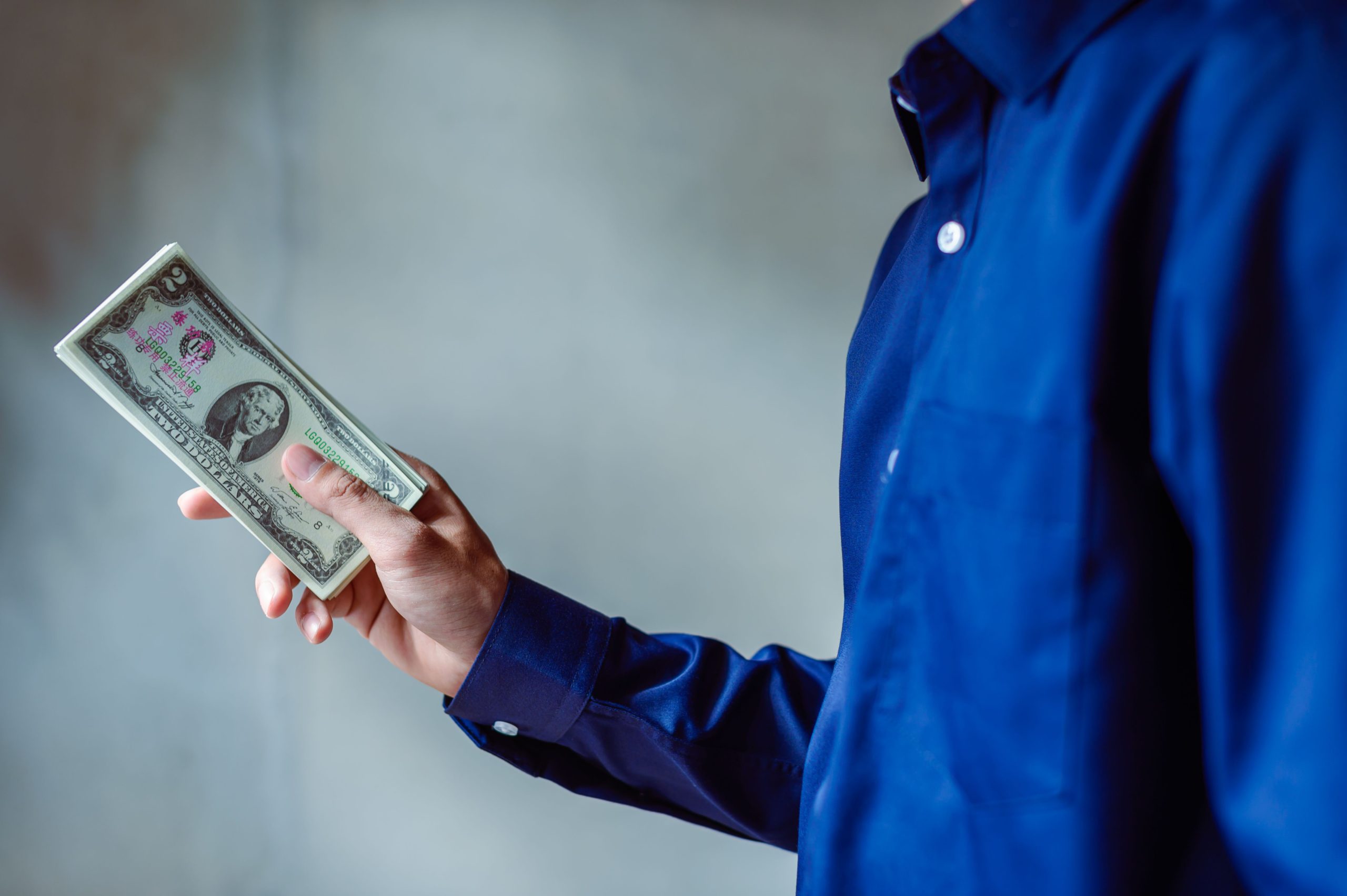 Homme en chemise bleue tenant une liasse de dollars